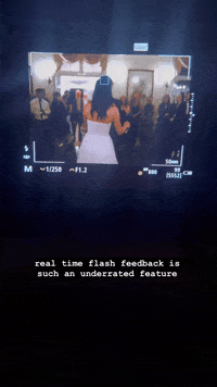 A camera screen displays a group of people at an indoor event, with a caption below reading, "real time flash feedback is such an underrated feature." Check out our Canon R1 Review to see how it excels in these moments.