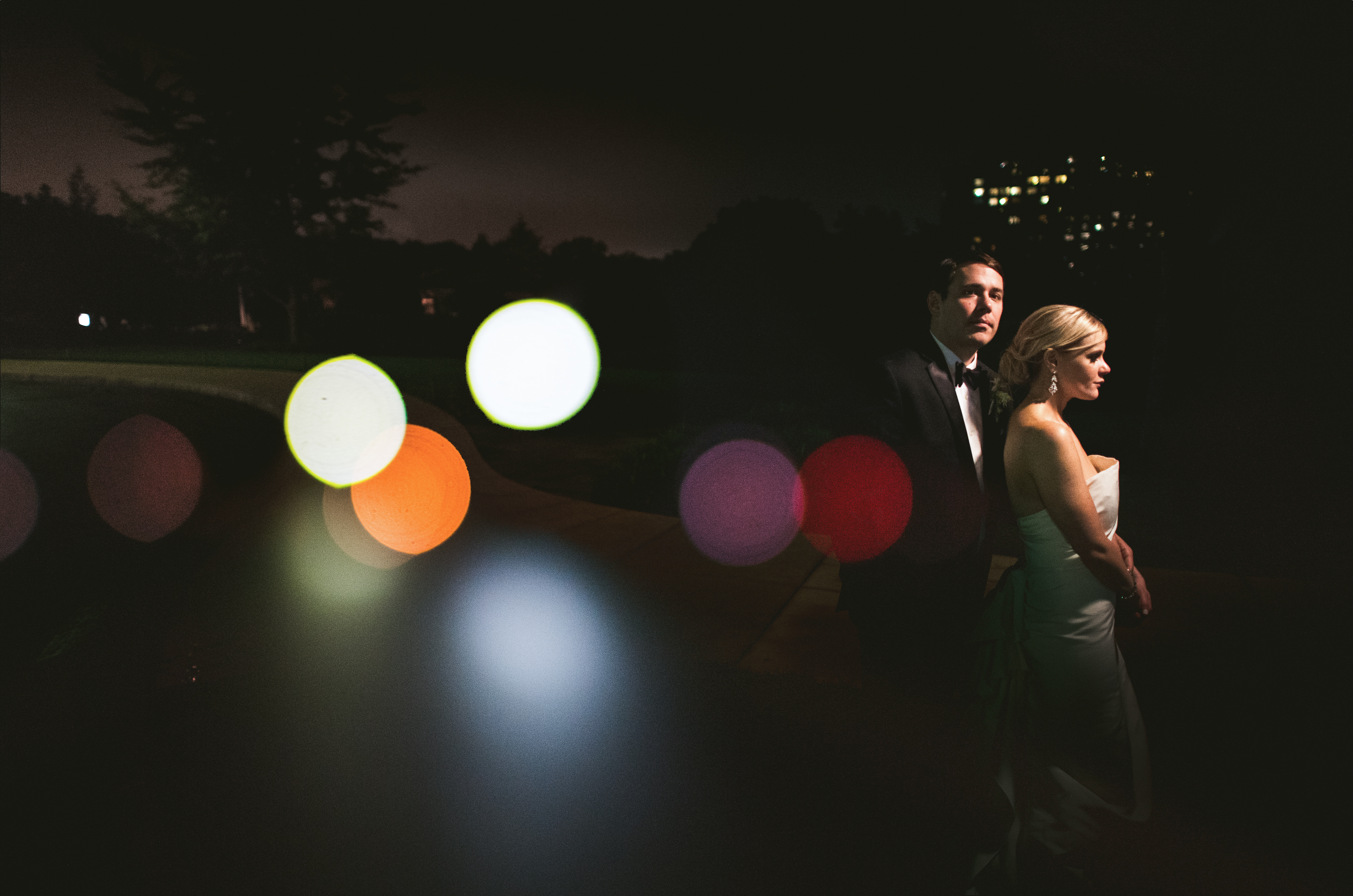 A couple in formal attire standing outdoors at night, with colorful bokeh lights in the foreground, featured in the FAQ section.