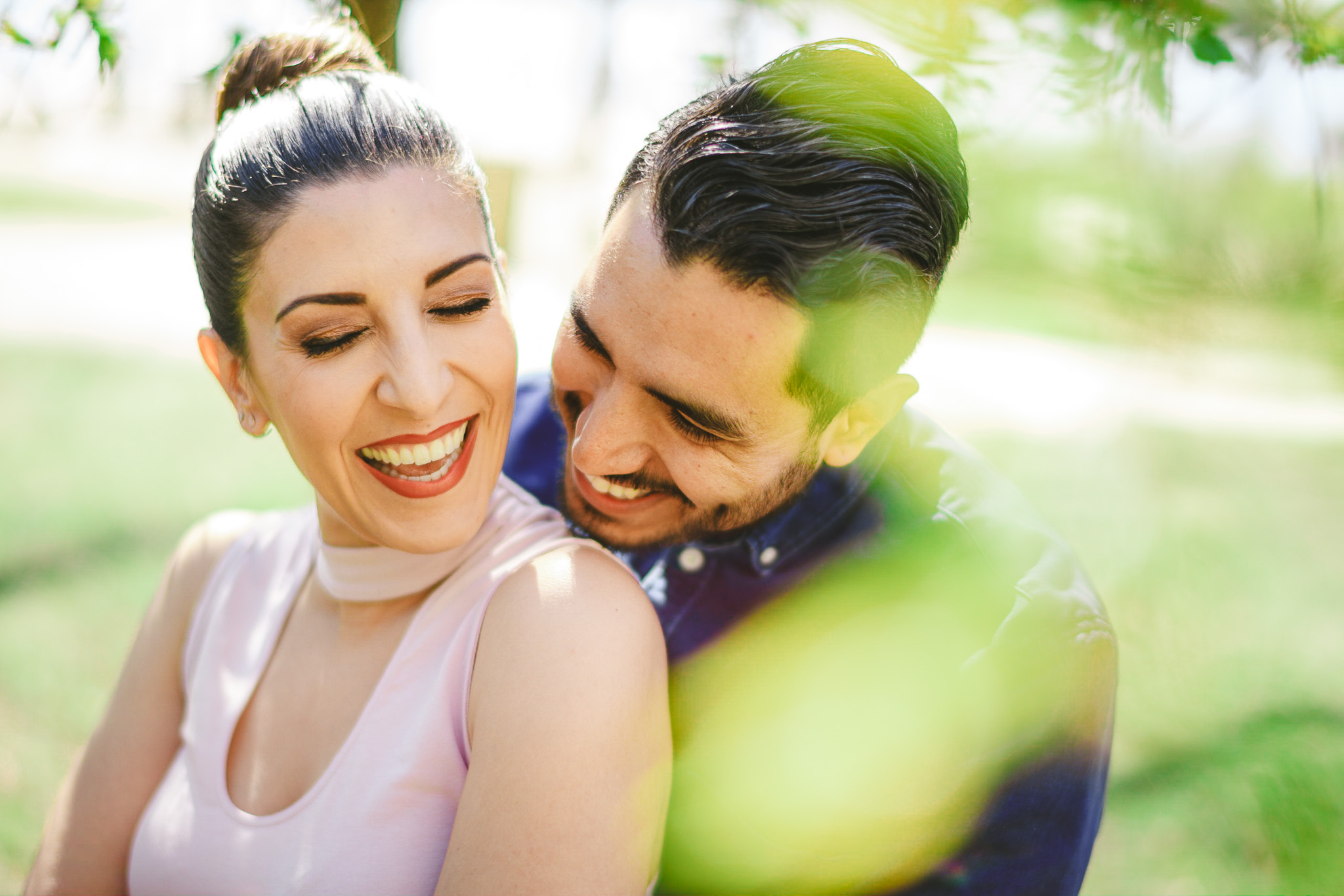 A woman and man smile and laugh together outdoors, with lush greenery in the background, capturing a perfect moment of happiness that photography can immortalize.