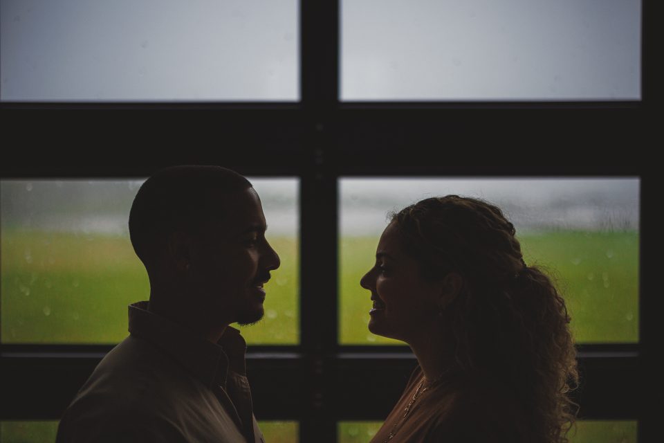 Silhouette of a man and woman facing each other in front of a window with a rainy landscape outside, as if captured by Auto Draft.