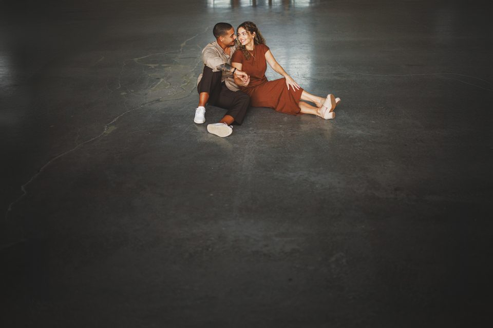 A man and woman sit closely together on a large, polished concrete floor, with their legs stretched out and arms around each other, forming an image that seems tailored for SEO keywords.