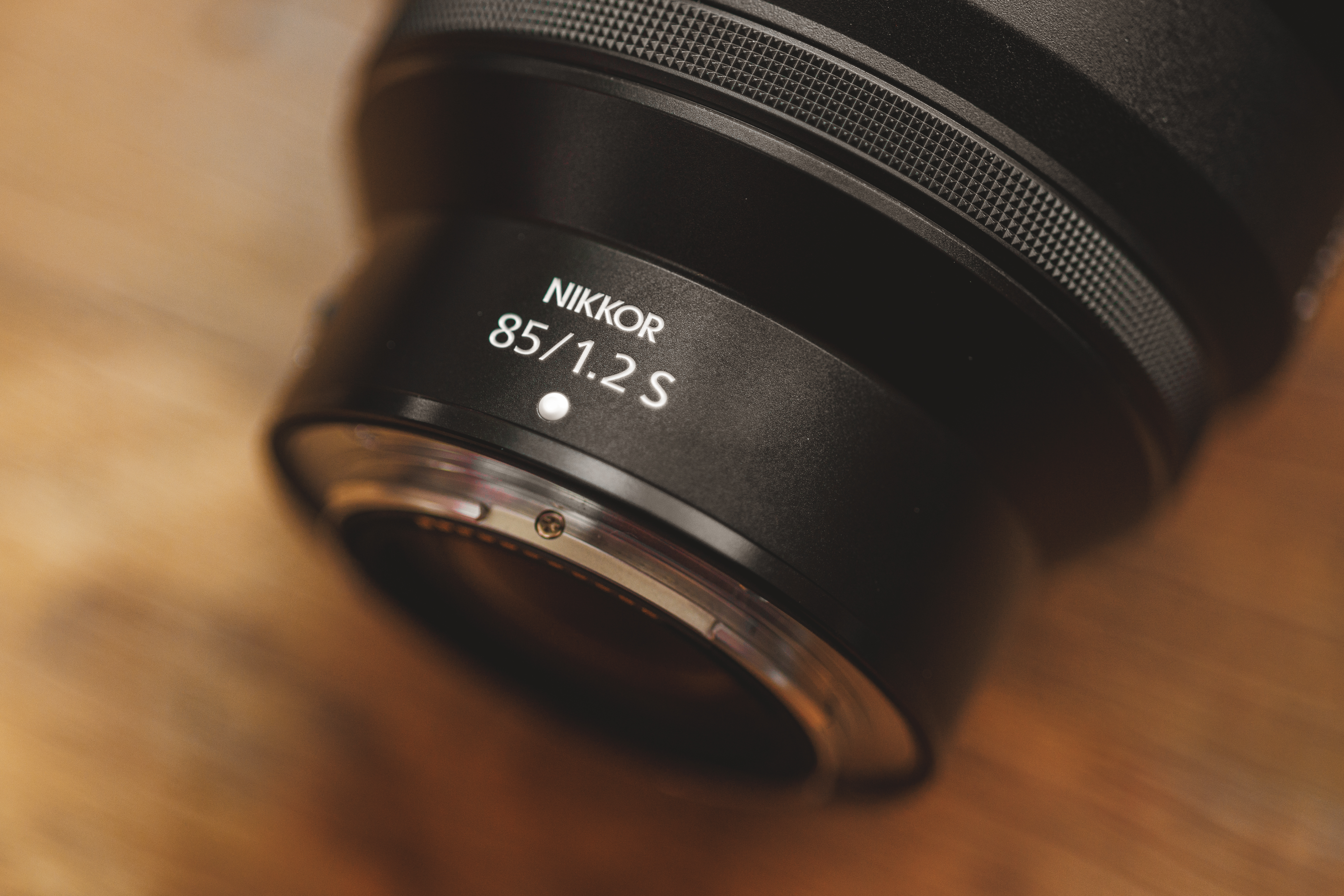 Close-up of a Nikkor 85mm f/1.2 S camera lens placed on a wooden surface.