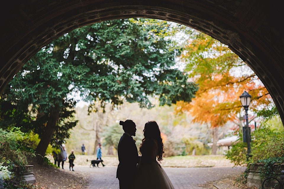 A silhouette of a bride and groom under an archway, framed by fall foliage at a boathouse wedding in NYC.