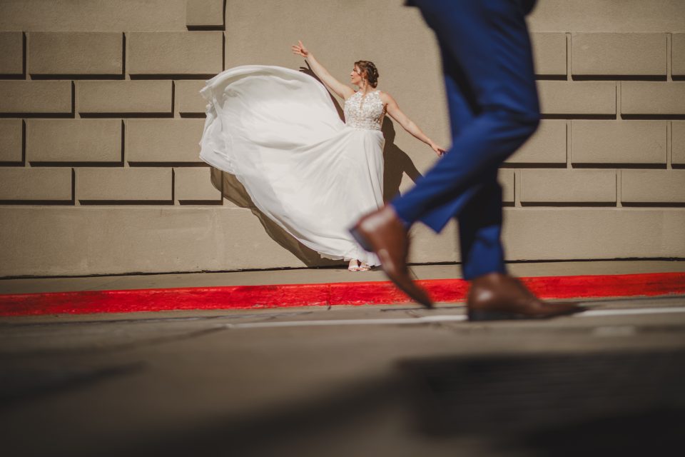 A bride in a flowing white dress twirls joyfully on a red carpet as a man in a blue suit walks by in the foreground, highlighting the FAQ section of their wedding brochure.