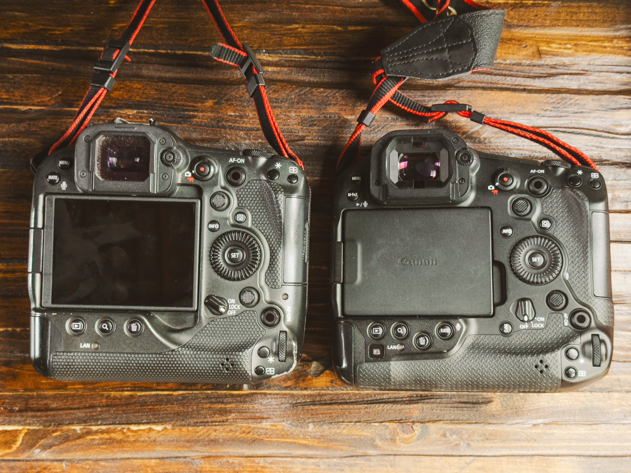Two professional Canon DSLR cameras with red straps are placed side by side on a wooden surface, showing their backs and various buttons—an ideal setup for a Canon R1 Review comparison.
