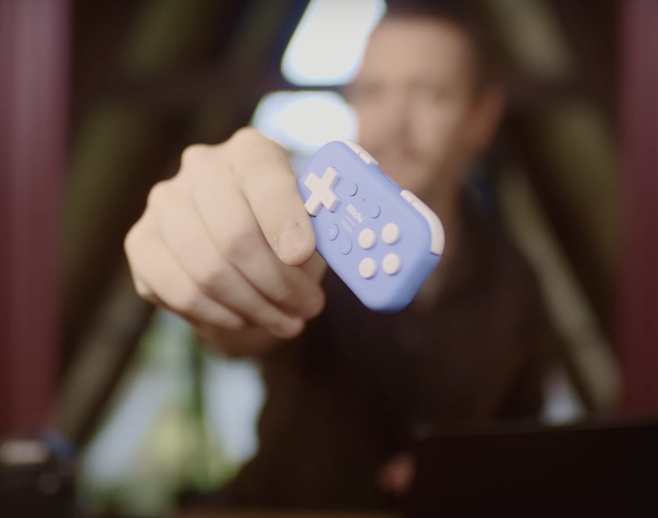Person holding a small blue and pink game controller towards the camera.